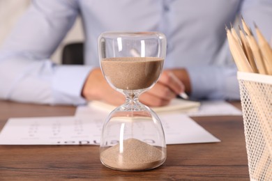 Photo of Deadline. Hourglass and man working at wooden table, selective focus