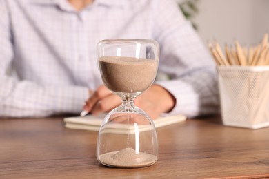 Photo of Deadline. Hourglass and man working at wooden table, selective focus