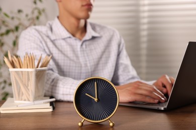 Photo of Deadline. Alarm clock and man working on laptop at wooden table, selective focus