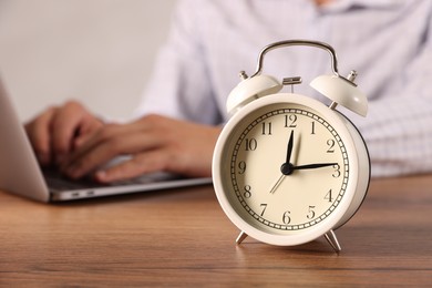 Photo of Deadline. Alarm clock and man working on laptop at wooden table, selective focus
