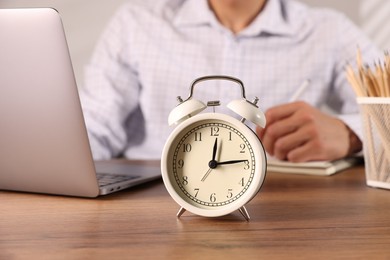 Photo of Deadline. Alarm clock and man working at wooden table, selective focus