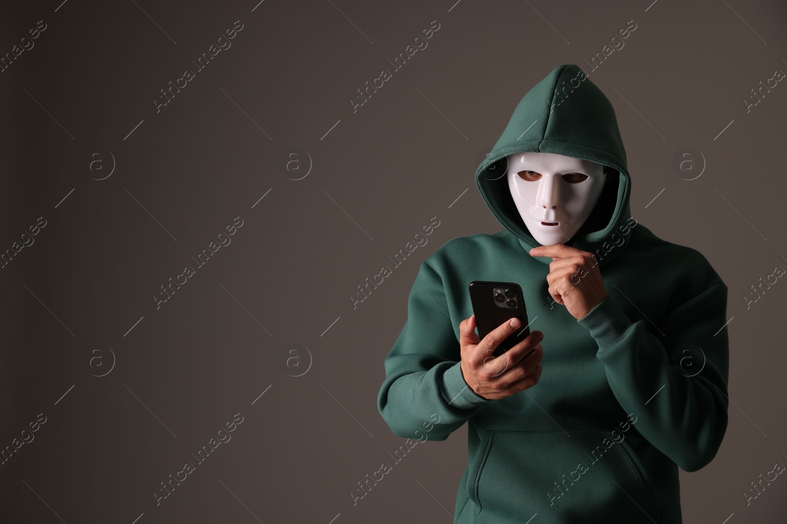 Photo of Anonymity. Masked man with smartphone on grey background, space for text