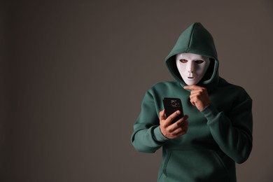 Photo of Anonymity. Masked man with smartphone on grey background, space for text