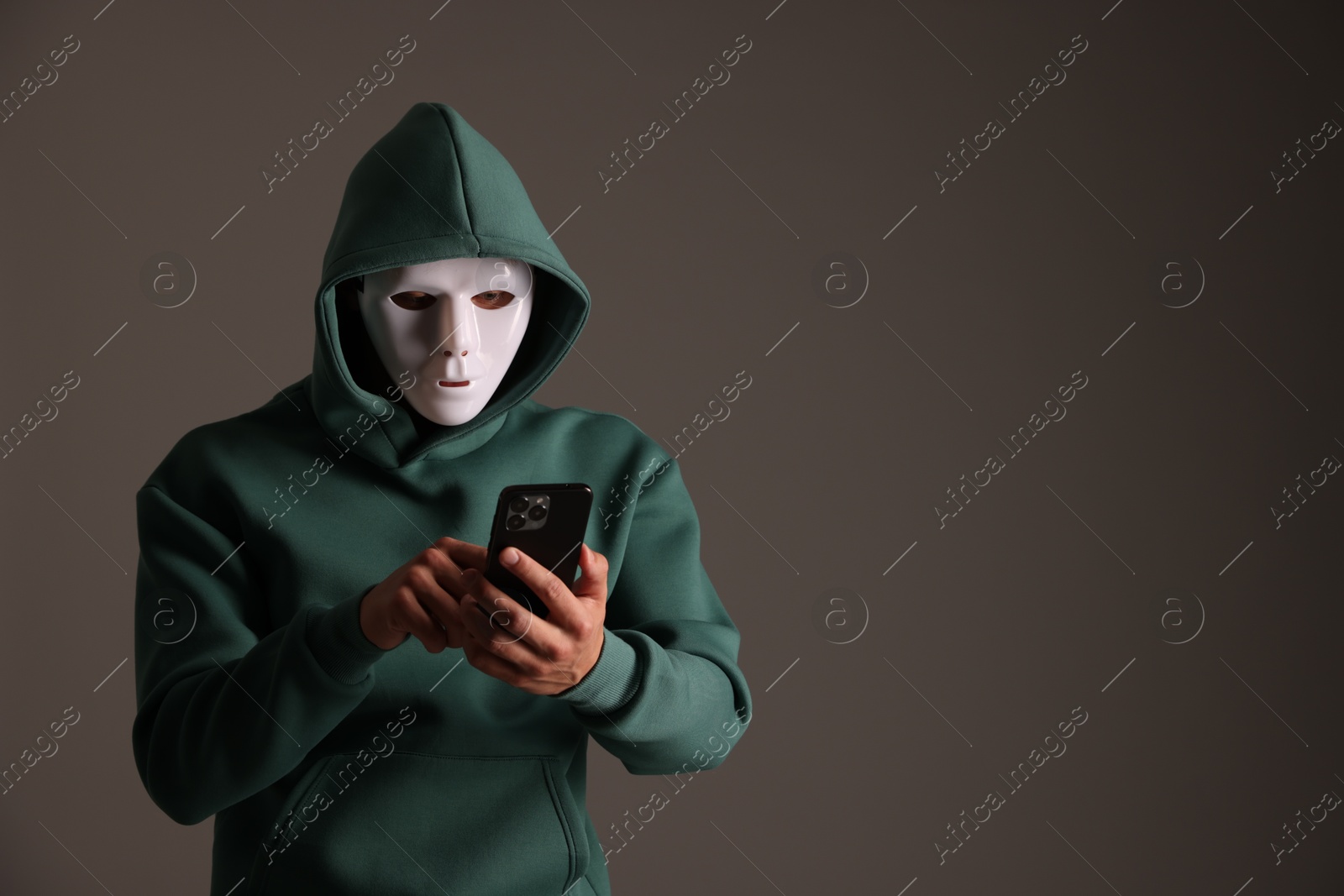 Photo of Anonymity. Masked man with smartphone on grey background, space for text