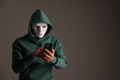 Photo of Anonymity. Masked man with smartphone on grey background, space for text