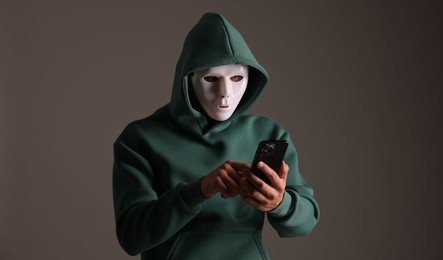 Photo of Anonymity. Masked man with smartphone on grey background