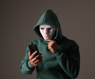 Photo of Anonymity. Masked man with smartphone on grey background