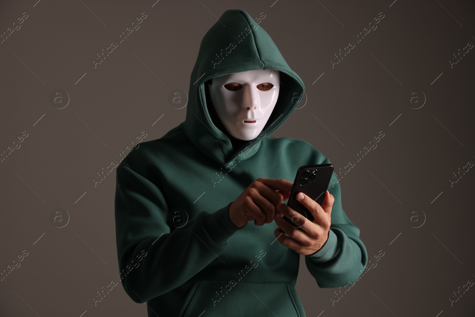 Photo of Anonymity. Masked man with smartphone on grey background