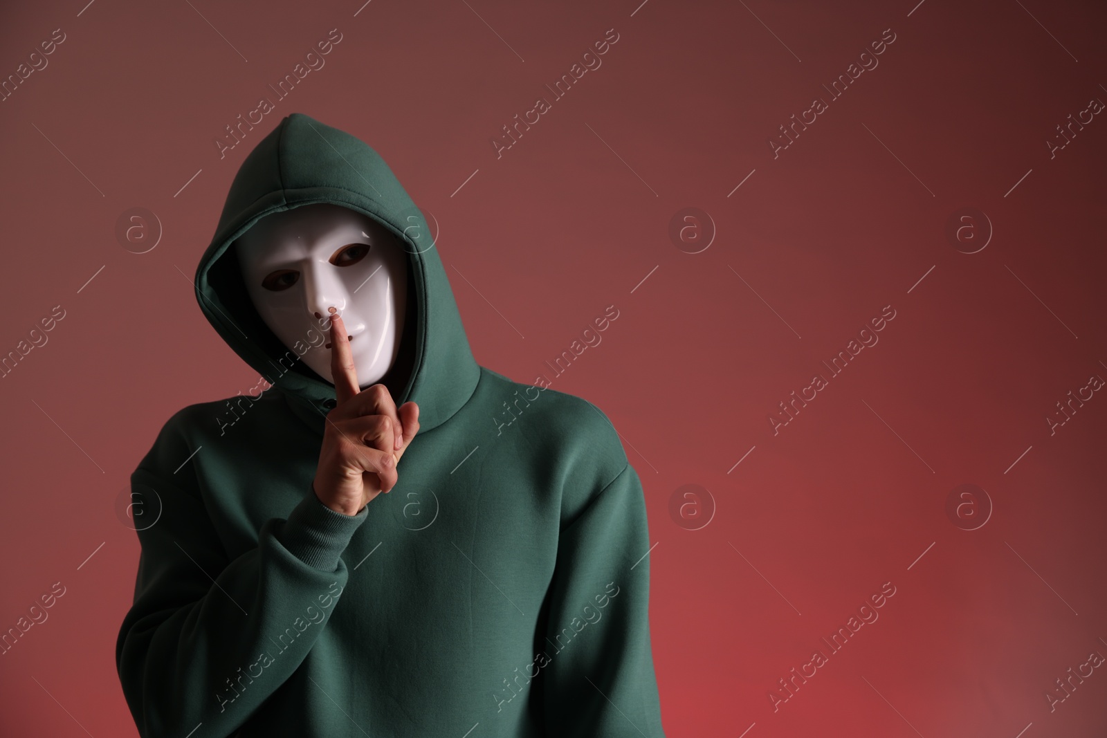 Photo of Anonymity. Man with mask showing hush gesture on red background, space for text