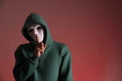 Photo of Anonymity. Man with mask showing hush gesture on red background, space for text