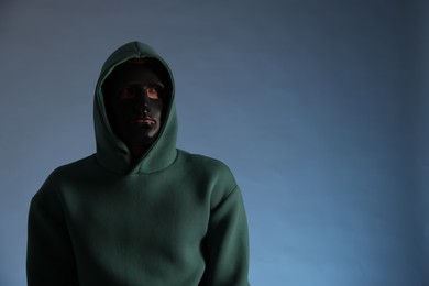 Photo of Anonymity. Man wearing mask on blue background, space for text