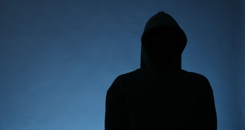 Photo of Silhouette of anonymous man in hood on blue background, space for text