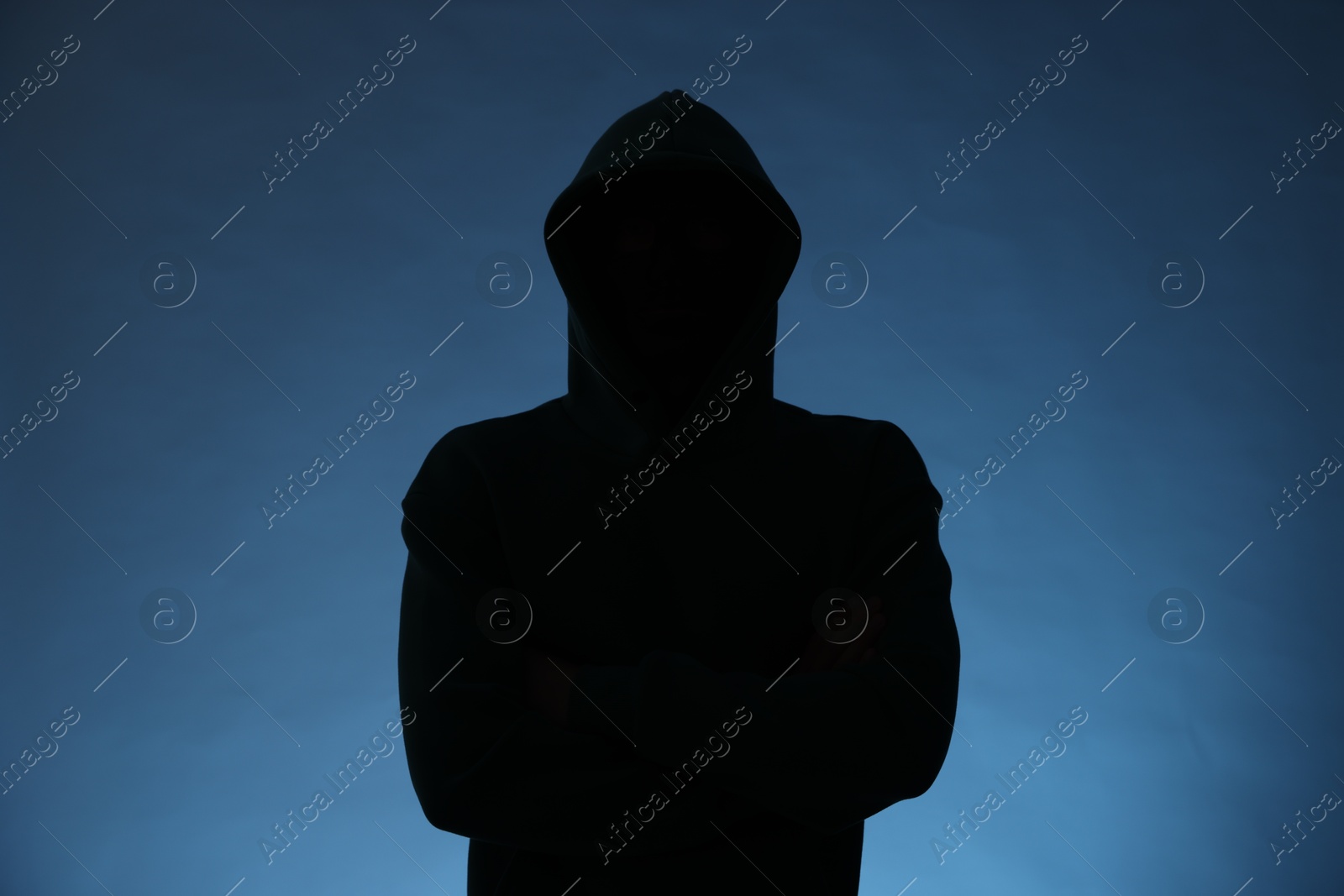 Photo of Silhouette of anonymous man in hood on blue background