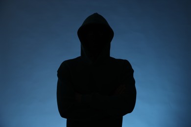 Photo of Silhouette of anonymous man in hood on blue background