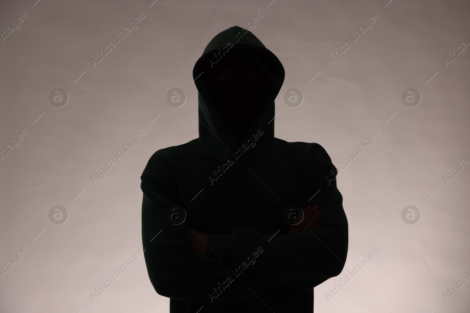 Photo of Silhouette of anonymous man in hood on grey background