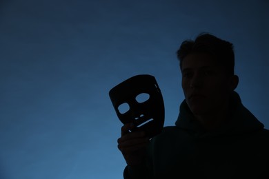 Photo of Anonymity. Silhouette of man with mask on blue background