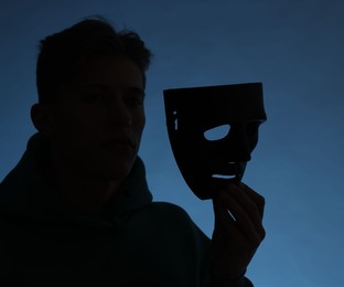 Photo of Anonymity. Silhouette of man with mask on blue background