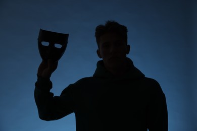 Photo of Anonymity. Silhouette of man with mask on blue background