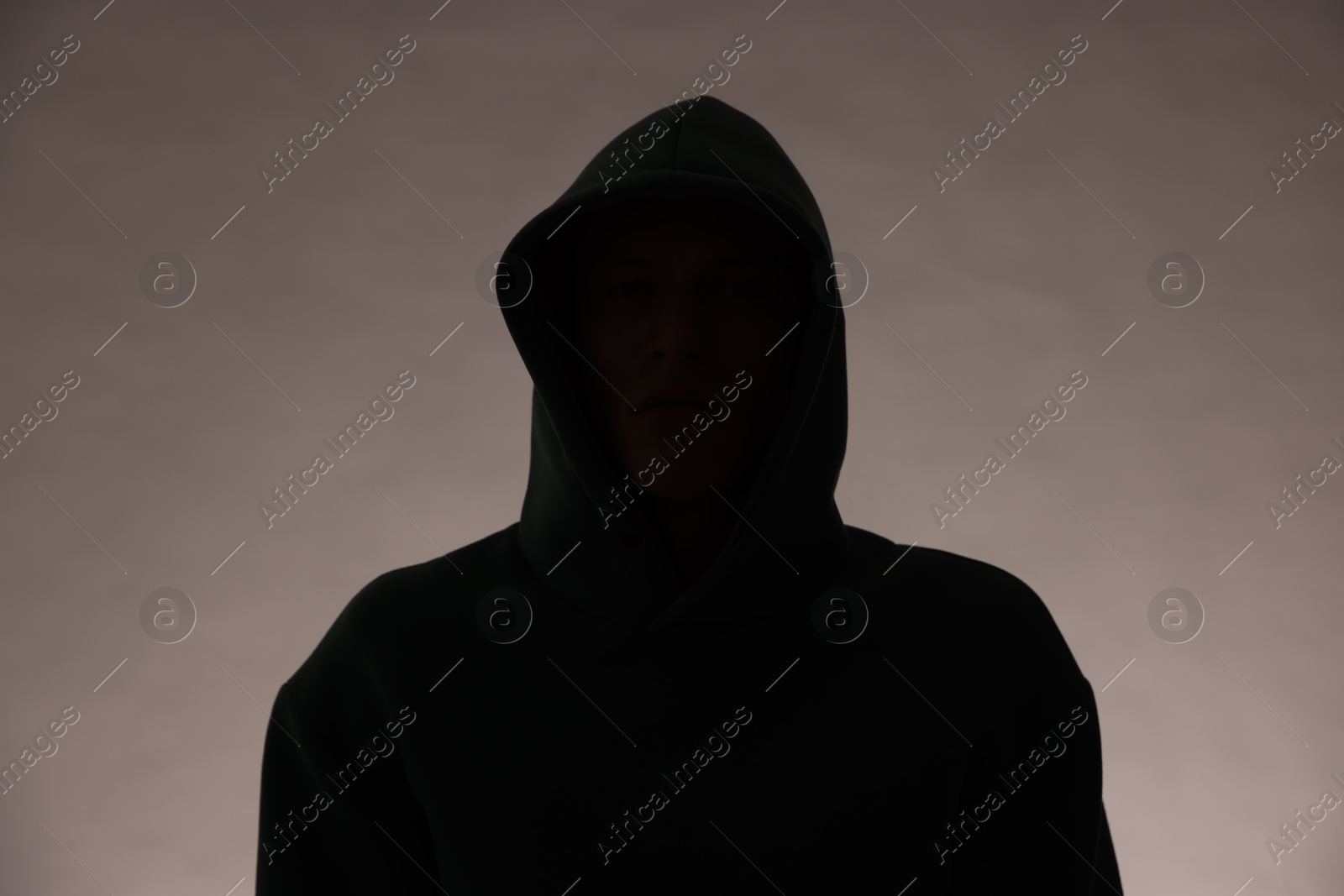 Photo of Silhouette of anonymous man in hood on grey background