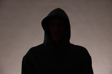 Photo of Silhouette of anonymous man in hood on grey background