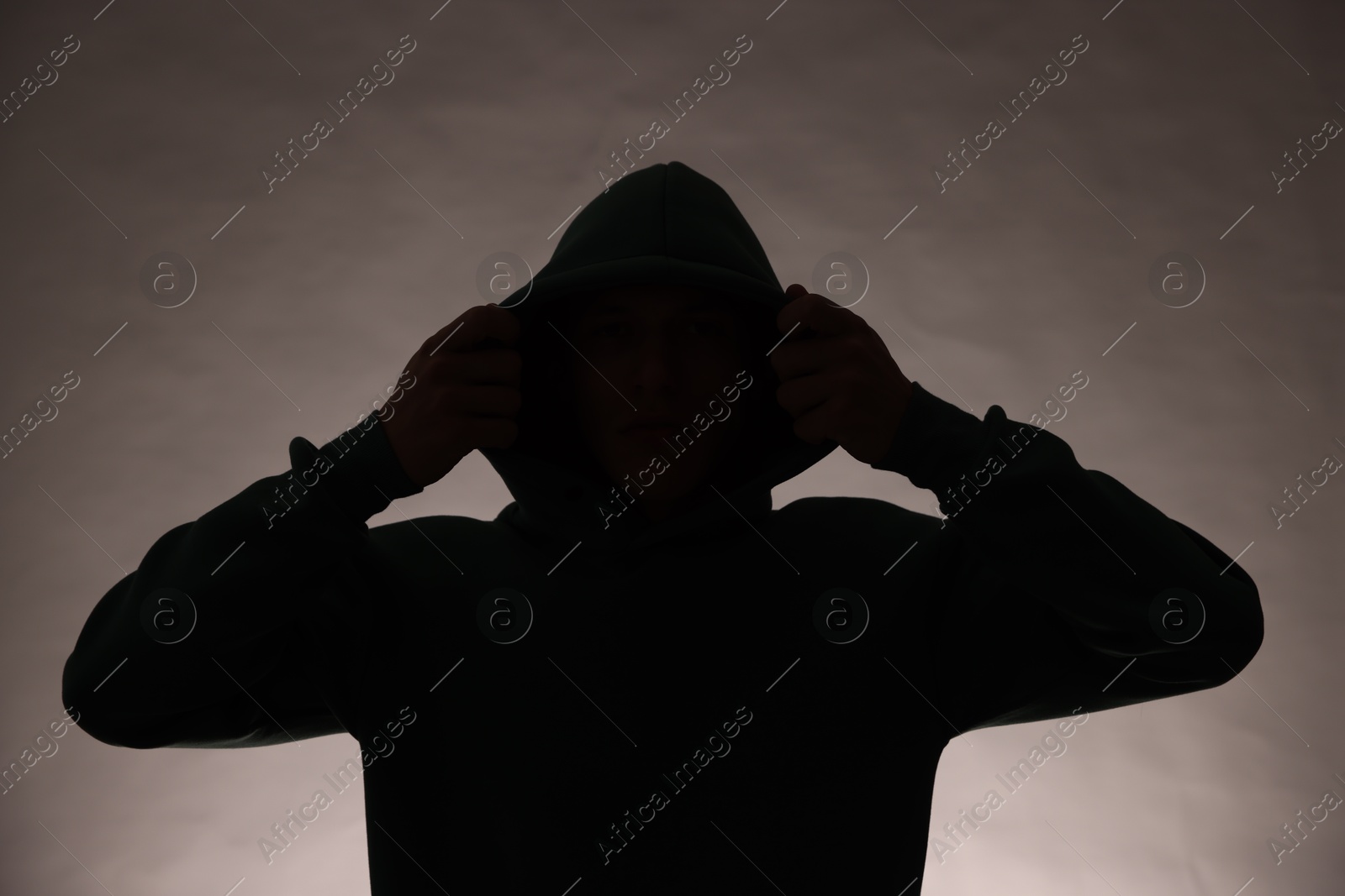 Photo of Silhouette of anonymous man in hood on grey background