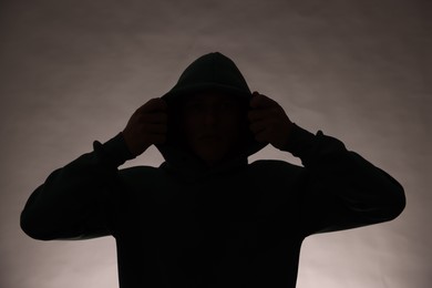 Photo of Silhouette of anonymous man in hood on grey background
