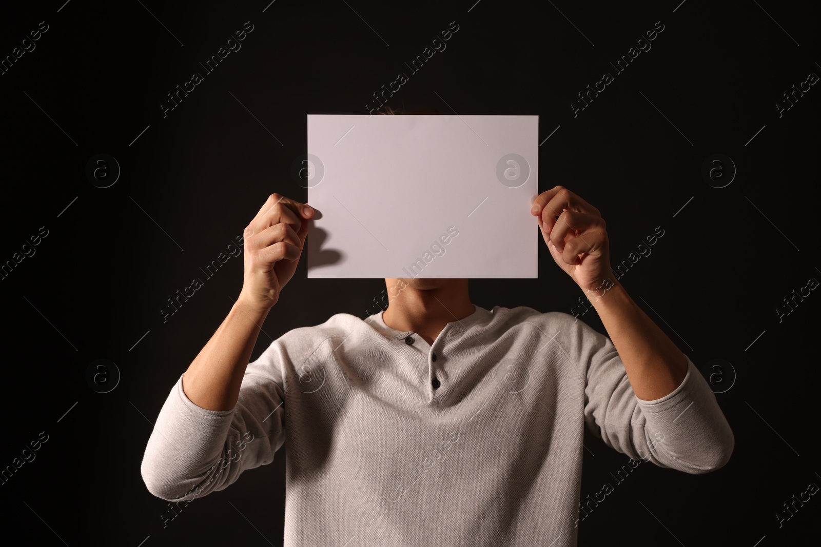 Photo of Man covering his face with paper sheet on dark background