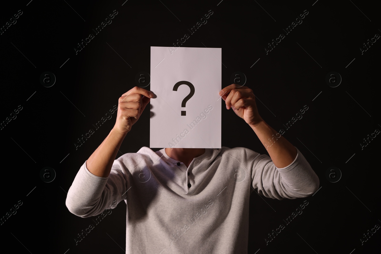 Photo of Man hiding behind paper sheet with question mark on dark background