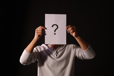 Photo of Man hiding behind paper sheet with question mark on dark background