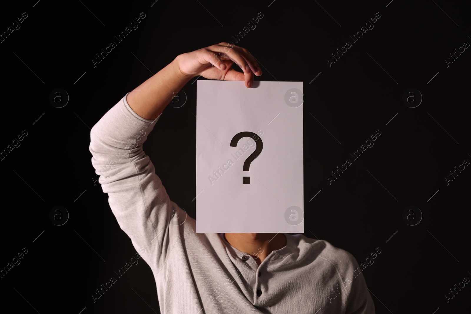Photo of Man hiding behind paper sheet with question mark on dark background