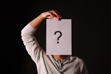 Photo of Man hiding behind paper sheet with question mark on dark background