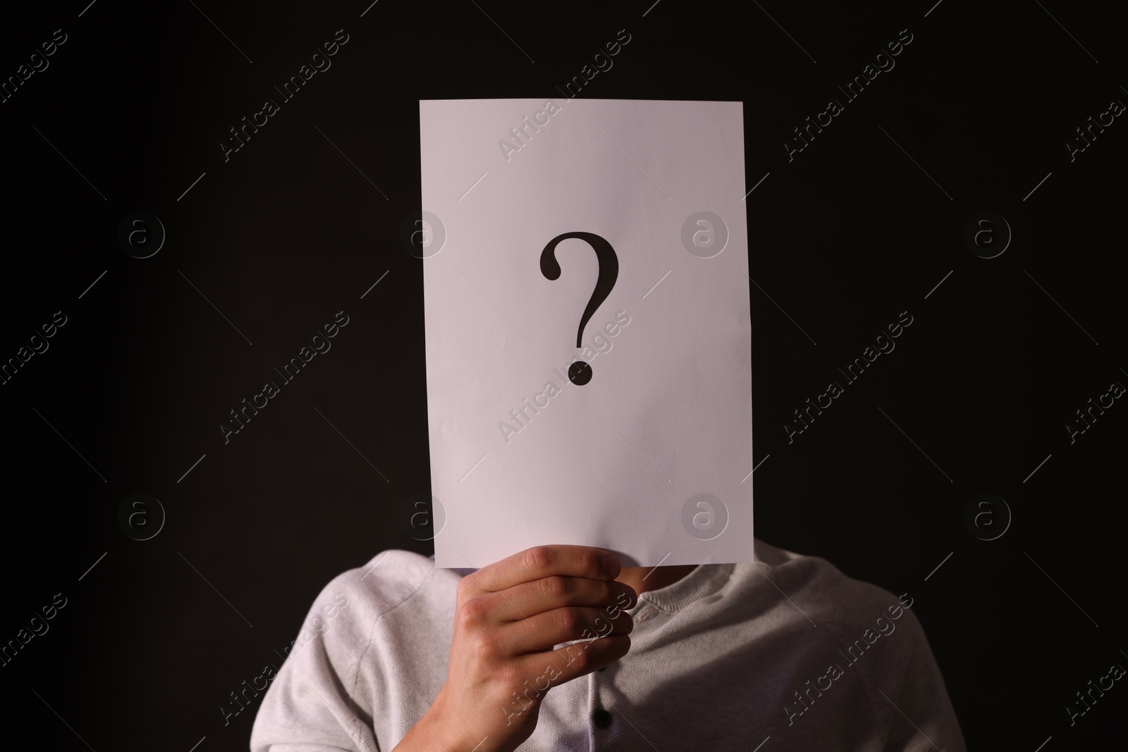Photo of Man hiding behind paper sheet with question mark on dark background
