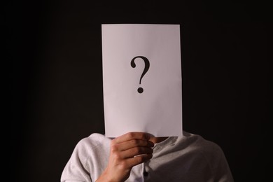 Photo of Man hiding behind paper sheet with question mark on dark background