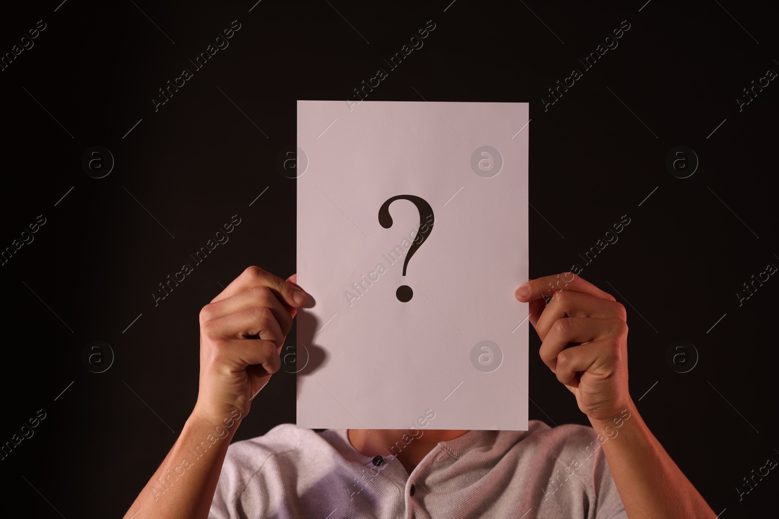 Photo of Man hiding behind paper sheet with question mark on dark background