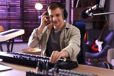Photo of Smiling man in headphones working with MIDI keyboard at table in home studio
