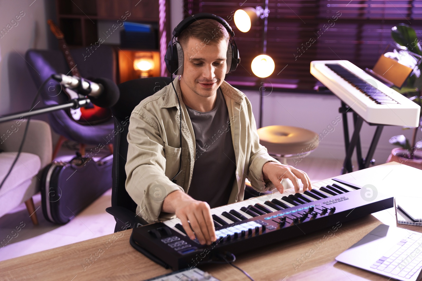 Photo of Man in headphones working with MIDI keyboard at table in home studio