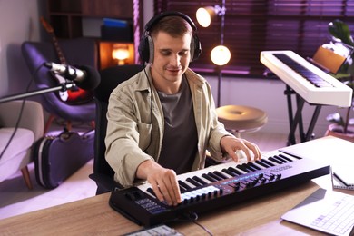 Photo of Man in headphones working with MIDI keyboard at table in home studio