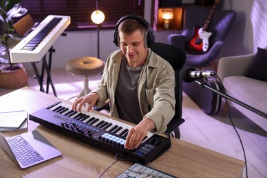 Photo of Man in headphones working with MIDI keyboard at table in home studio