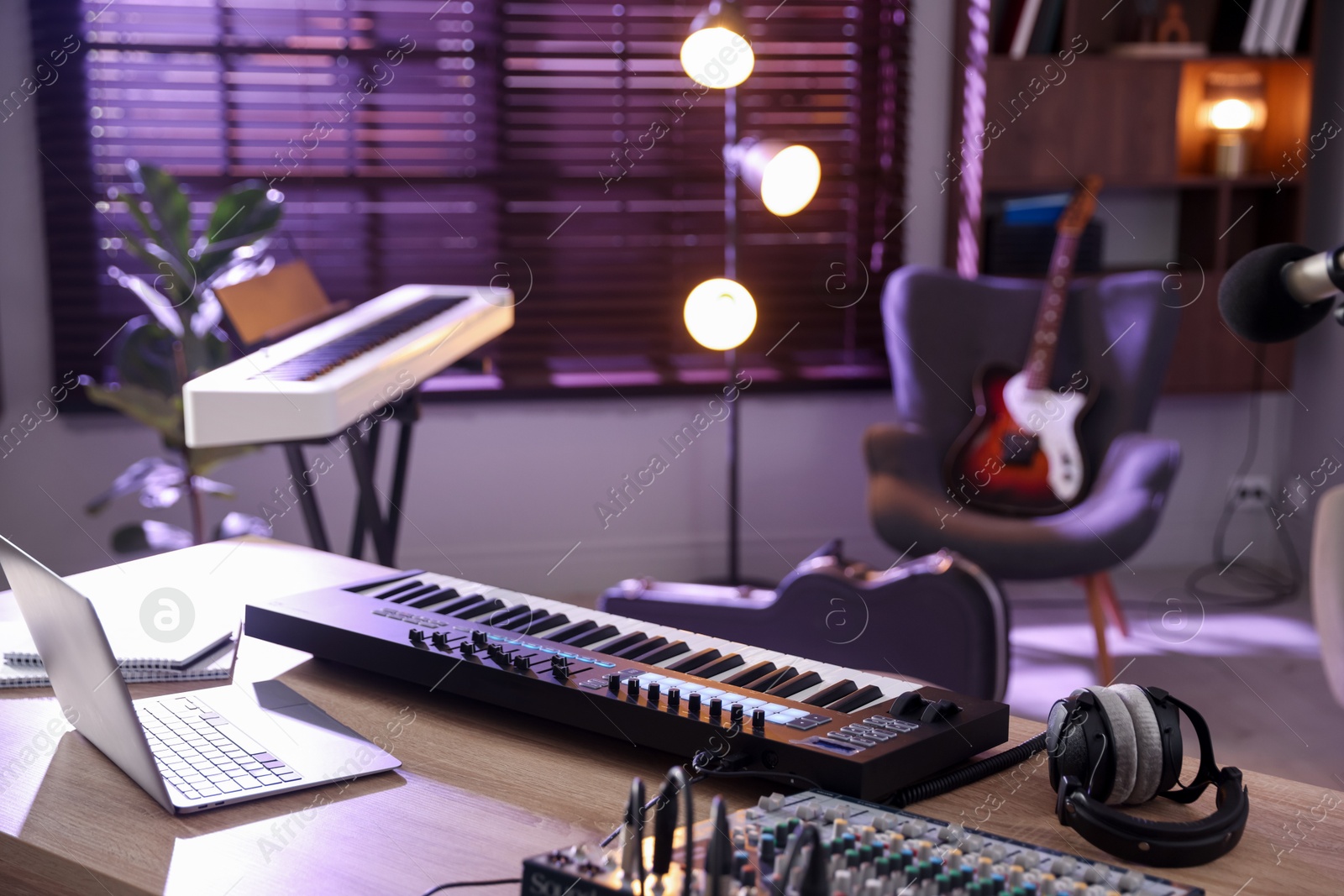 Photo of MIDI keyboard, laptop and headphones on wooden table in home studio