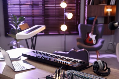 Photo of MIDI keyboard, laptop and headphones on wooden table in home studio