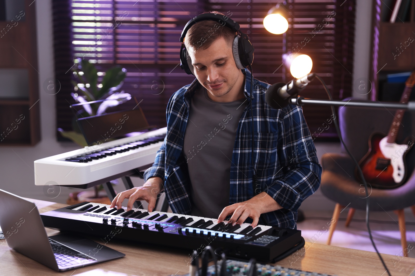 Photo of Man in headphones working with MIDI keyboard at table in home studio