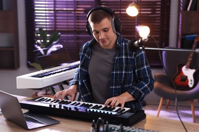 Photo of Man in headphones working with MIDI keyboard at table in home studio