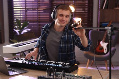 Photo of Man in headphones working with MIDI keyboard and microphone at table in home studio