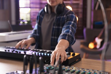 Photo of Man working with MIDI keyboard and dj mixer at table, selective focus