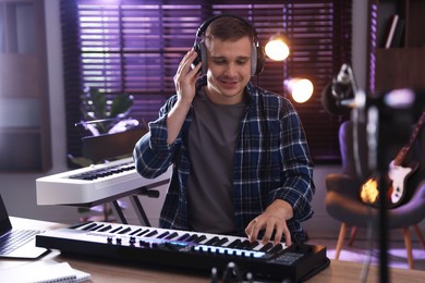 Photo of Smiling man in headphones working with MIDI keyboard at table in home studio