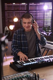 Photo of Smiling man in headphones working with MIDI keyboard at table in home studio