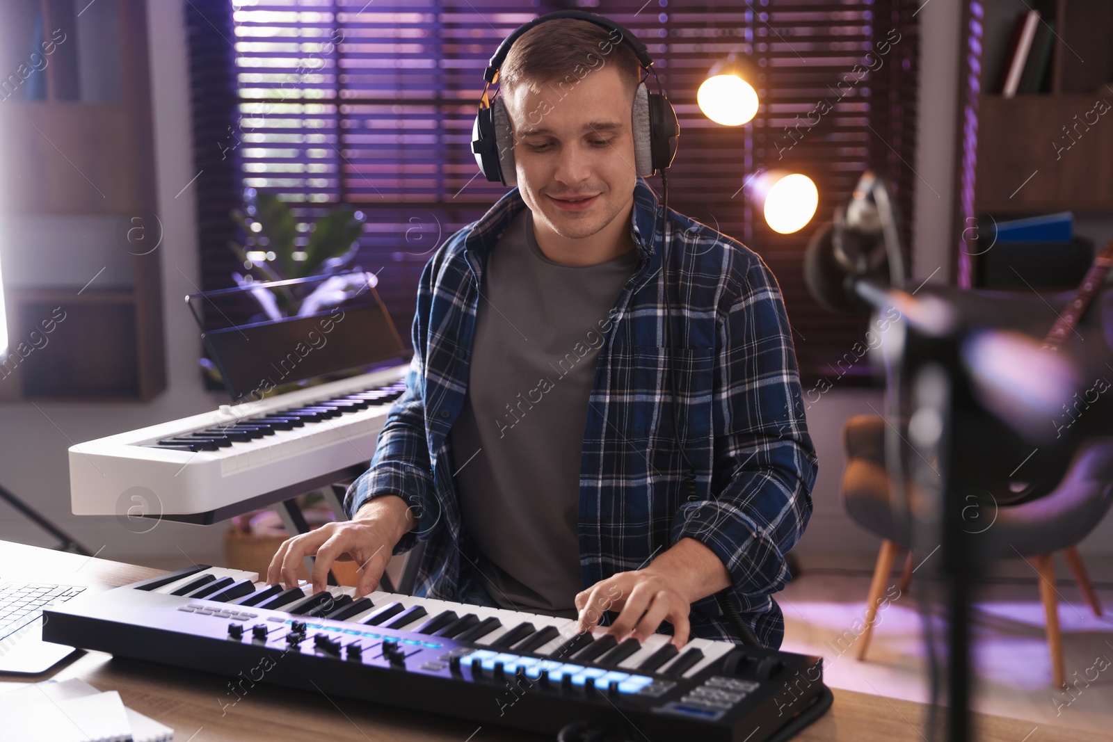 Photo of Smiling man in headphones working with MIDI keyboard at table in home studio