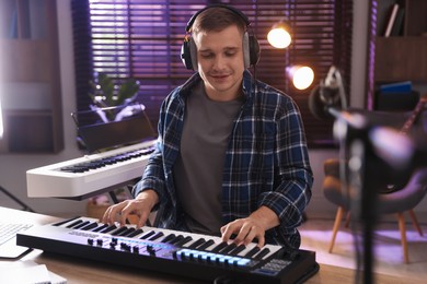 Photo of Smiling man in headphones working with MIDI keyboard at table in home studio