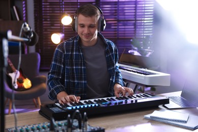 Photo of Man in headphones working with MIDI keyboard at table in home studio