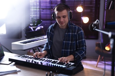 Photo of Man in headphones working with MIDI keyboard at table in home studio